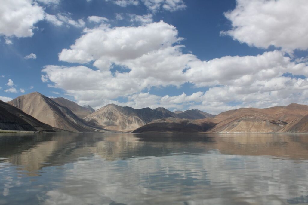 Tranquil mountain lake reflecting a clear blue sky with clouds.