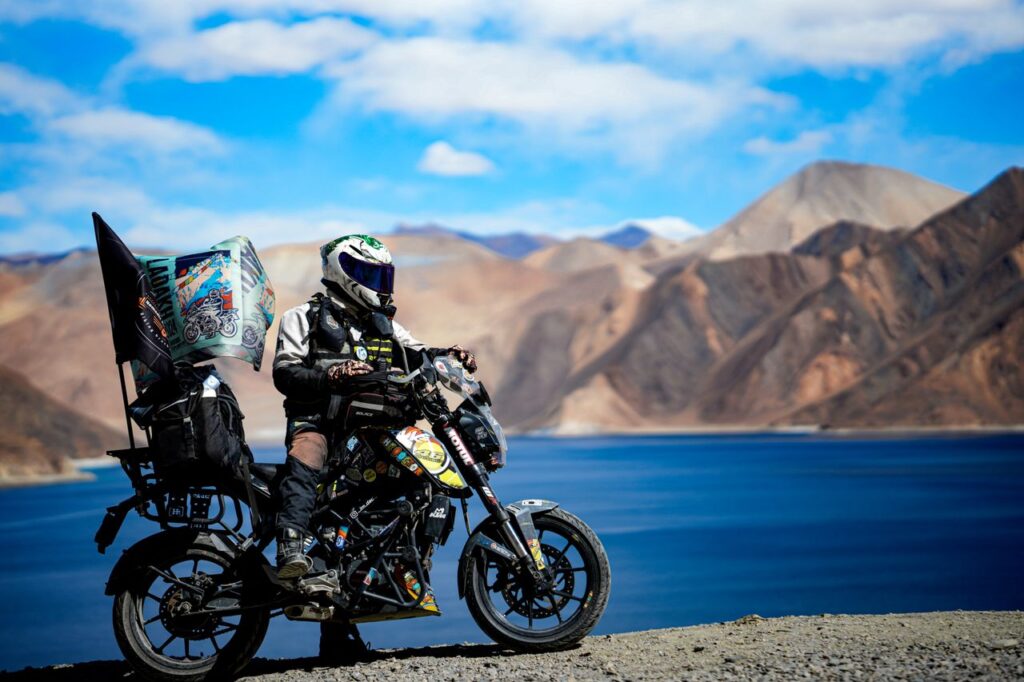 A biker on a motorcycle trip through scenic Ladakh, capturing the stunning Pangong Lake.